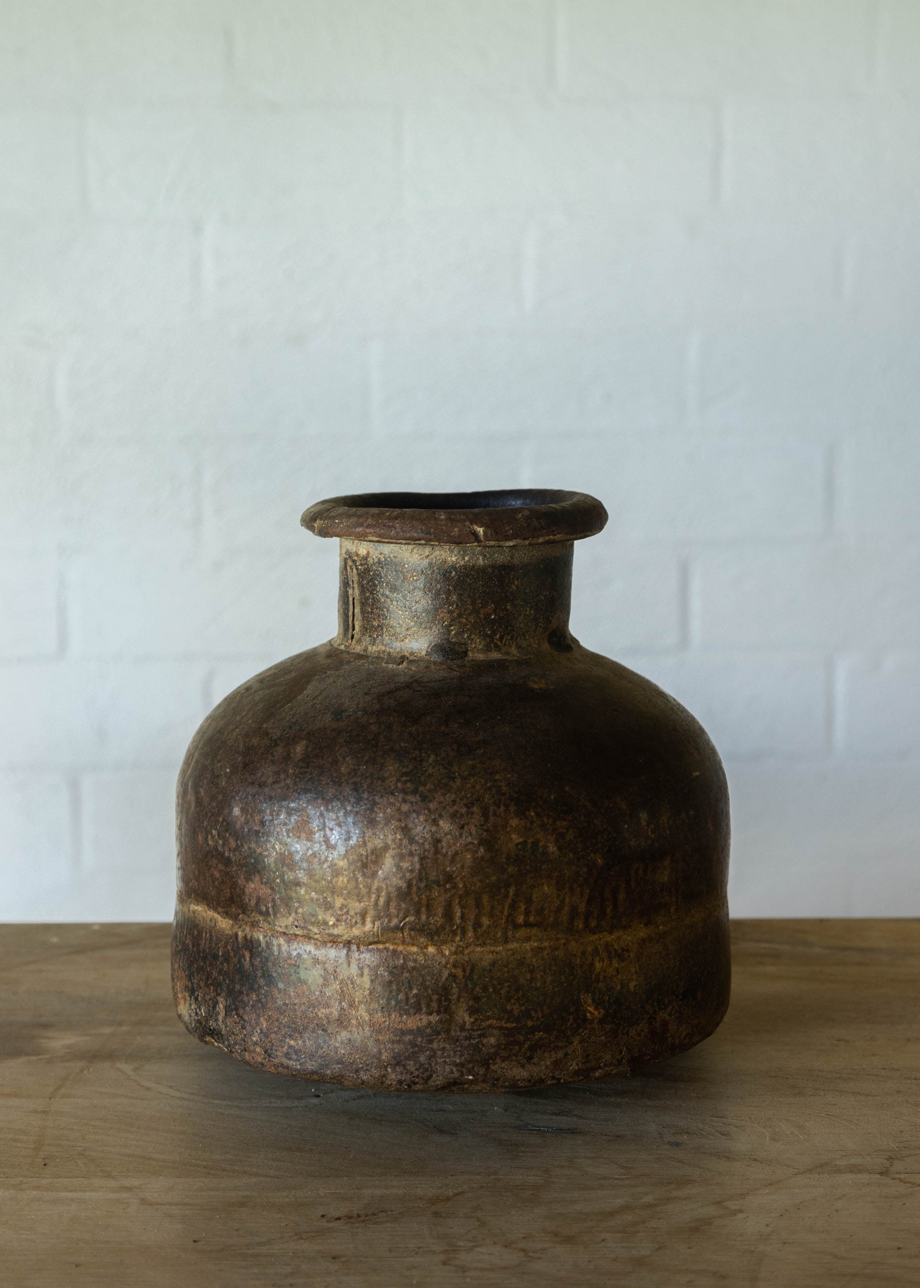 Rustic iron pot from India with a large base, a narrow neck and  a turned lip at the opening. Width and height equal at approx 30cm. 