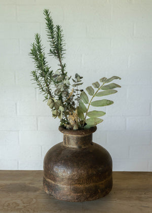 Rustic iron pot from India with a large base, a narrow neck and  a turned lip at the opening. Width and height equal at approx 30cm. Green foliage displayed.