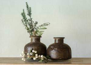 Rustic iron pot from India with a large base, a narrow neck and  a turned lip at the opening. Width and height equal at approx 30cm. Green foliage displayed.