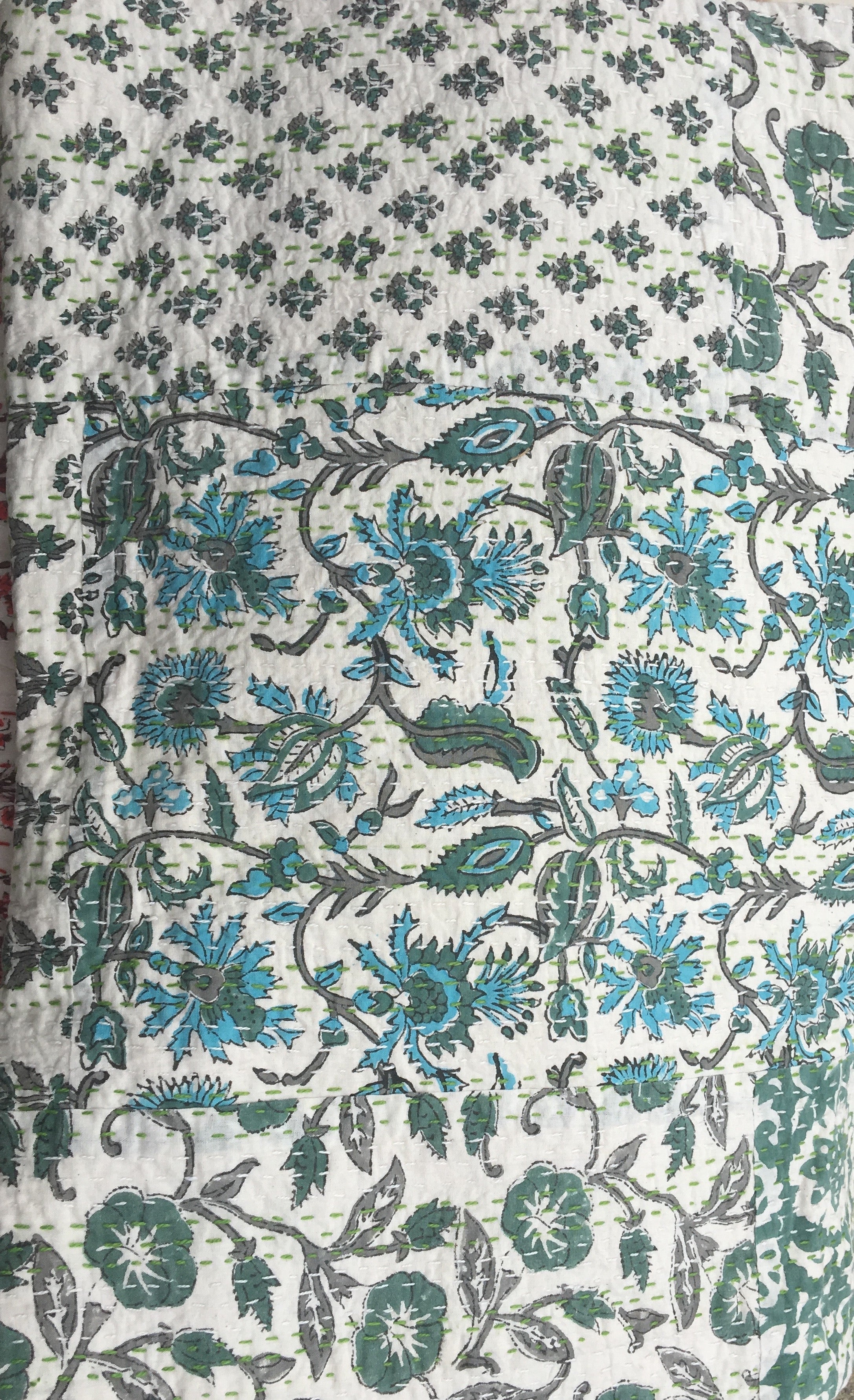 A close up image of 100% cotton Kantha quilt with flower pattern in  different green colours on a white background.  The kantha quilt is a hand made textile from India, traditionally created as a wedding quilt and is hand stitched throughout.  