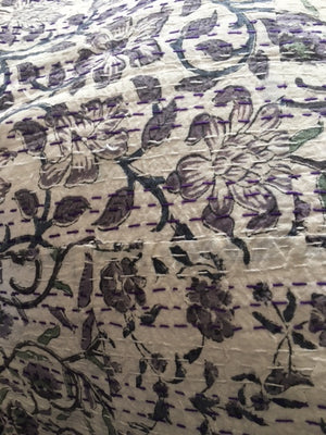 A close up image of 100% cotton Kantha quilt with flower pattern in lavender and green on a white background.  The kantha quilt is a hand made textile from India, traditionally created as a wedding quilt and is hand stitched throughout.  