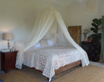 A king size 100% cotton mosquito net hoop style , in a bedroom, organic natural colour  with 2 side openings. 