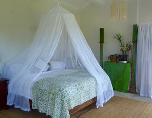 A king size 100% cotton mosquito net hoop style , in a bedroom, predominantly white, with 2 side openings. 