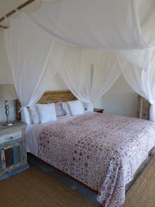 100% cotton Kantha quilt with flower pattern in pink and green on a white background. The kantha quilt is displayed on a king sized with pillows and a cotton mosquito net draped above. The kantha quilt is a hand made textile from India, traditionally created as a wedding quilt and is hand stitched throughout.  
