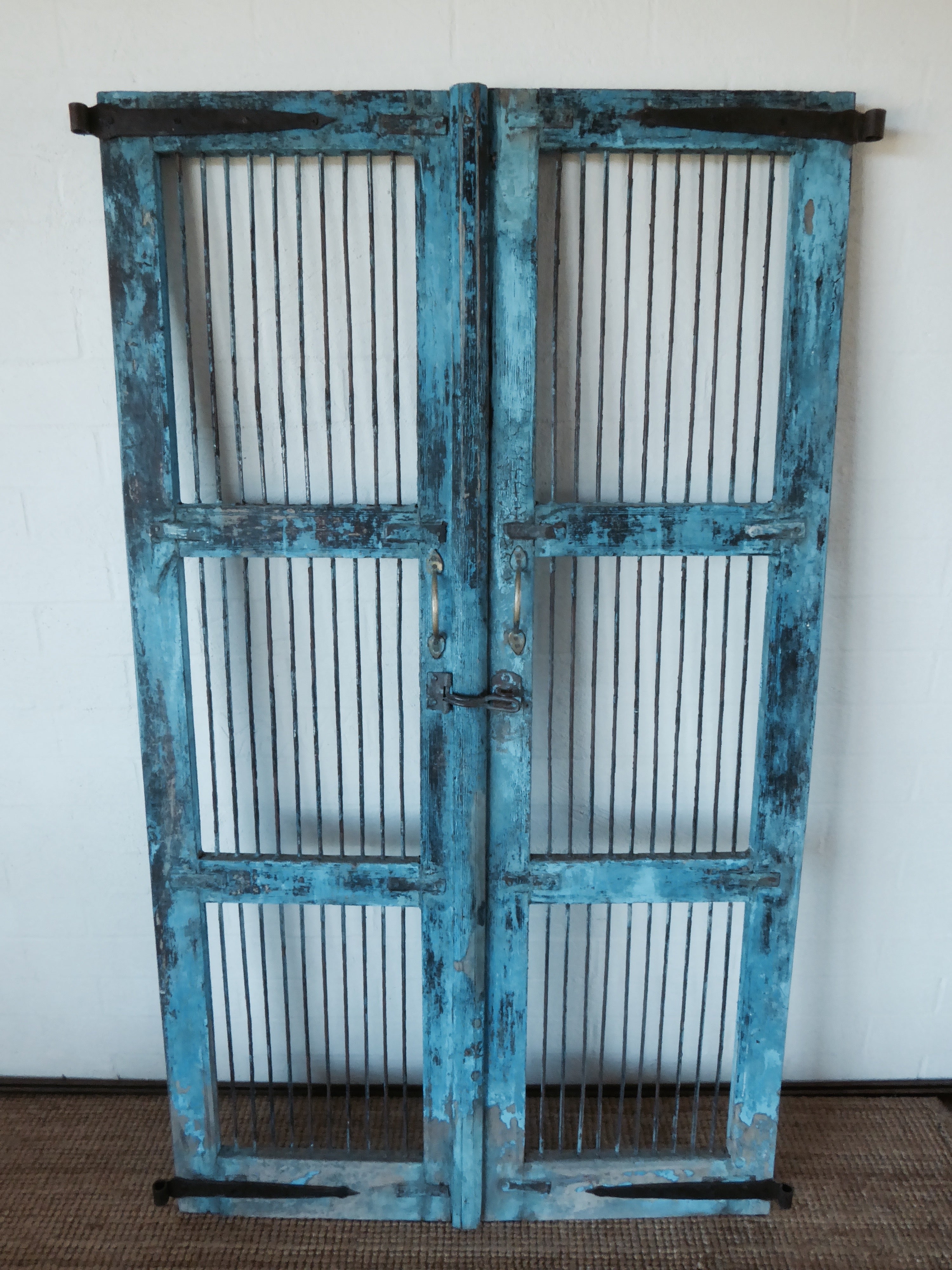 Solid teak gates from India. Rustic blue  paint finish and vertical iron bars in 3 timber framed sections. Solid iron hinges on the sides of the door at the top and bottom. Iron latch, brass handles  and iron details . Perfect for securing pets, homes and children. Good outside as garden gates.