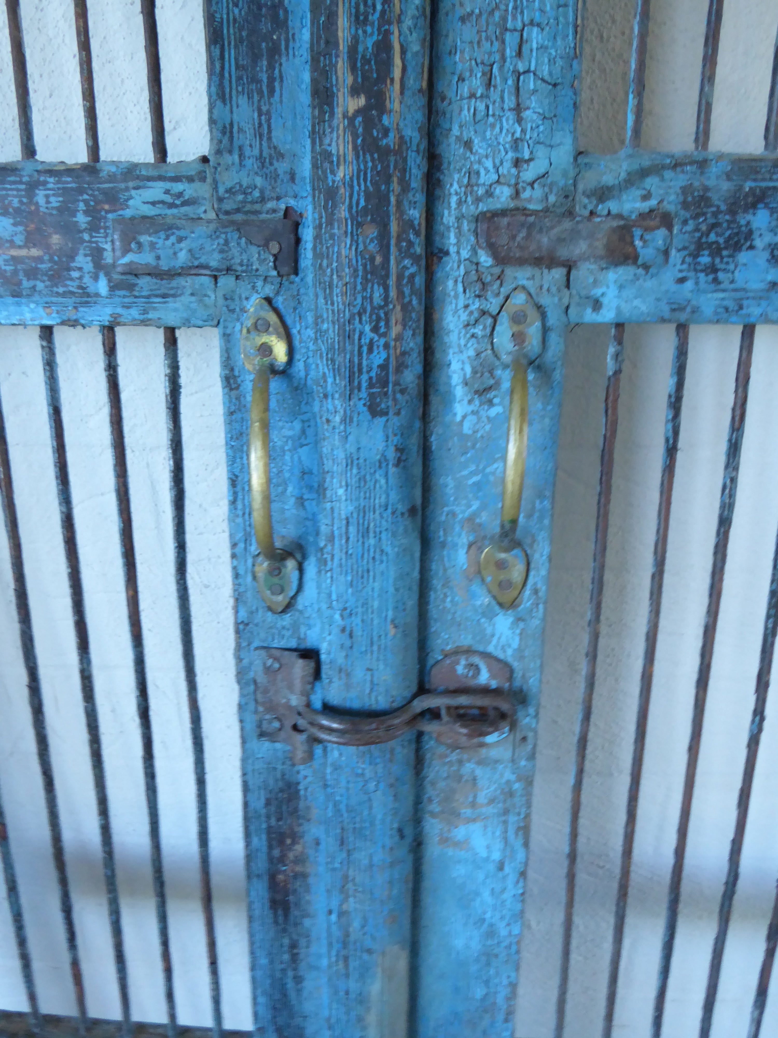 Close up image of solid teak gates from India. Rustic blue  paint finish and vertical iron bars. Iron latch, brass handles  and iron details . Perfect for securing pets, homes and children. Good outside as garden gates.