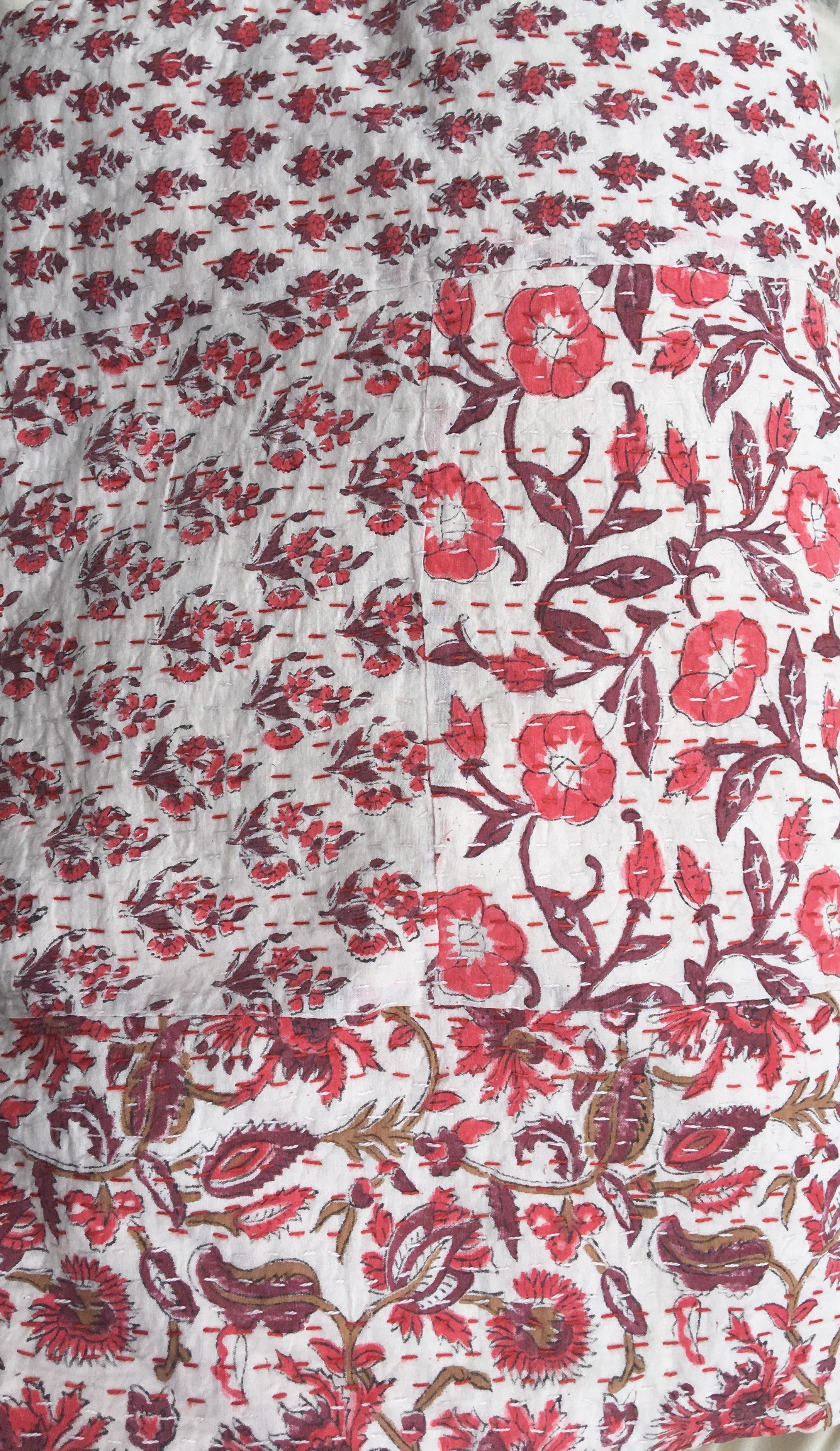 A close up image of 100% cotton Kantha quilt with flower pattern in burgundy and reds on a white background.  The kantha quilt is a hand made textile from India, traditionally created as a wedding quilt and is hand stitched throughout.  