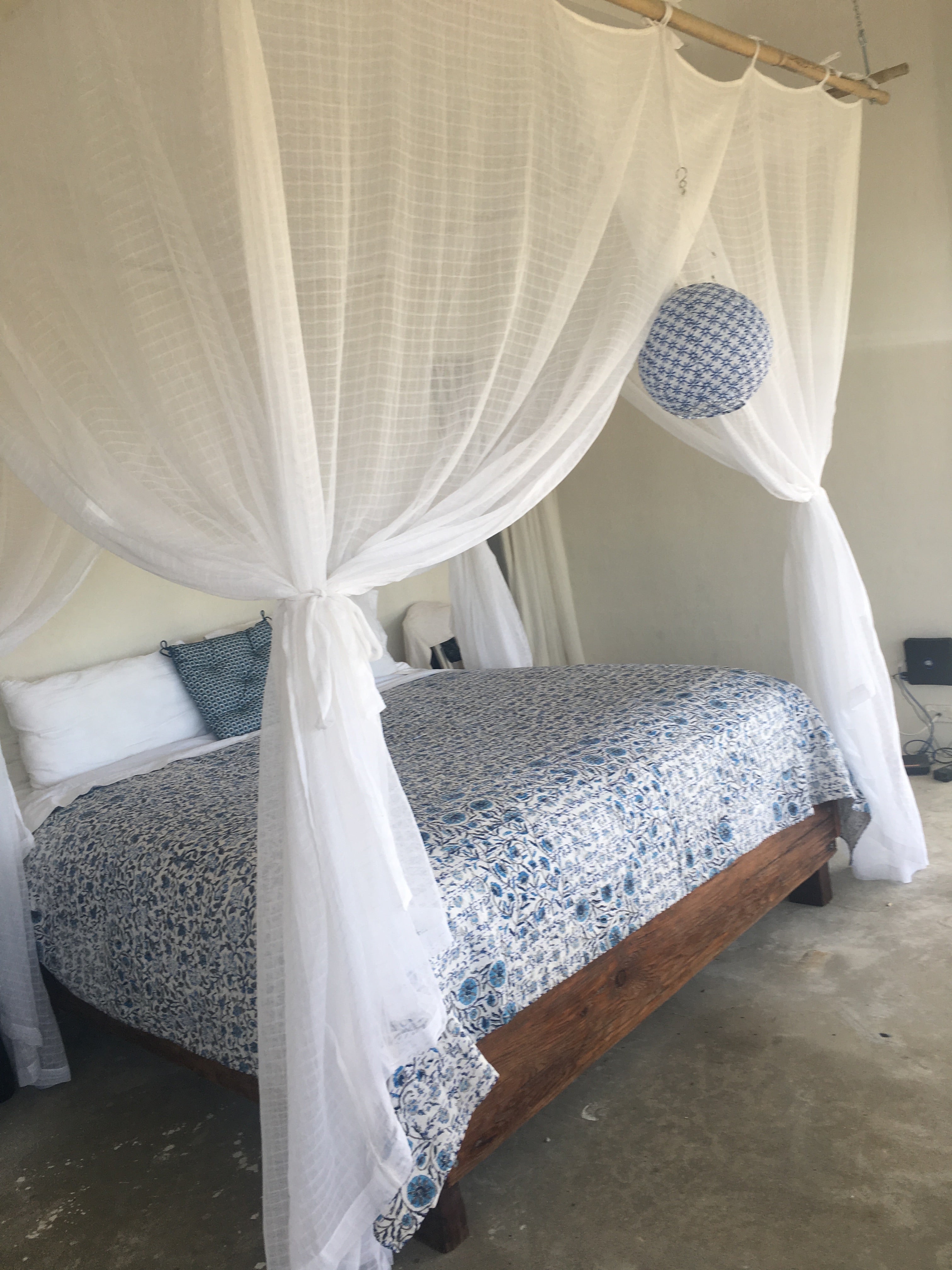 100% cotton Kantha quilt with flower pattern in blue on a white background. The kantha quilt is displayed on a king sized with pillows and a cotton mosquito net draped above. The kantha quilt is a hand made textile from India, traditionally created as a wedding quilt and is hand stitched throughout.  